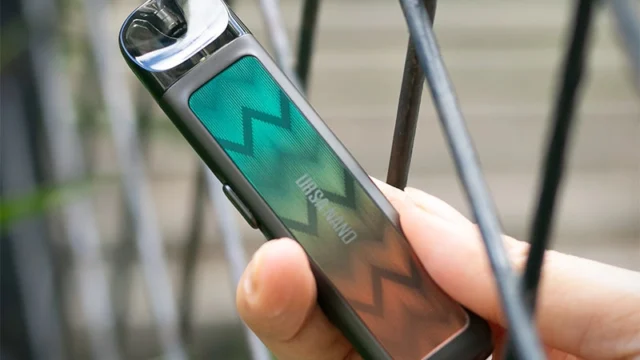 A hand holding an original Lost Vape URSA NANO beside a metal railing, with the model name visible.