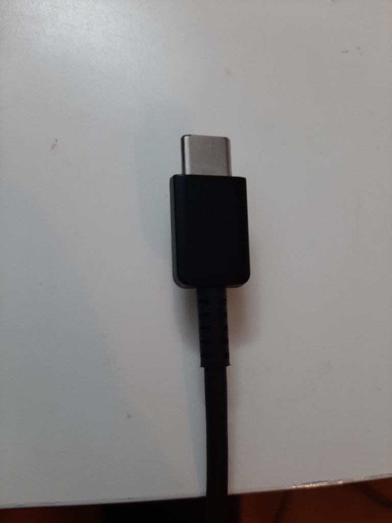 A black USB-C cable plug lying on a light-coloured surface.